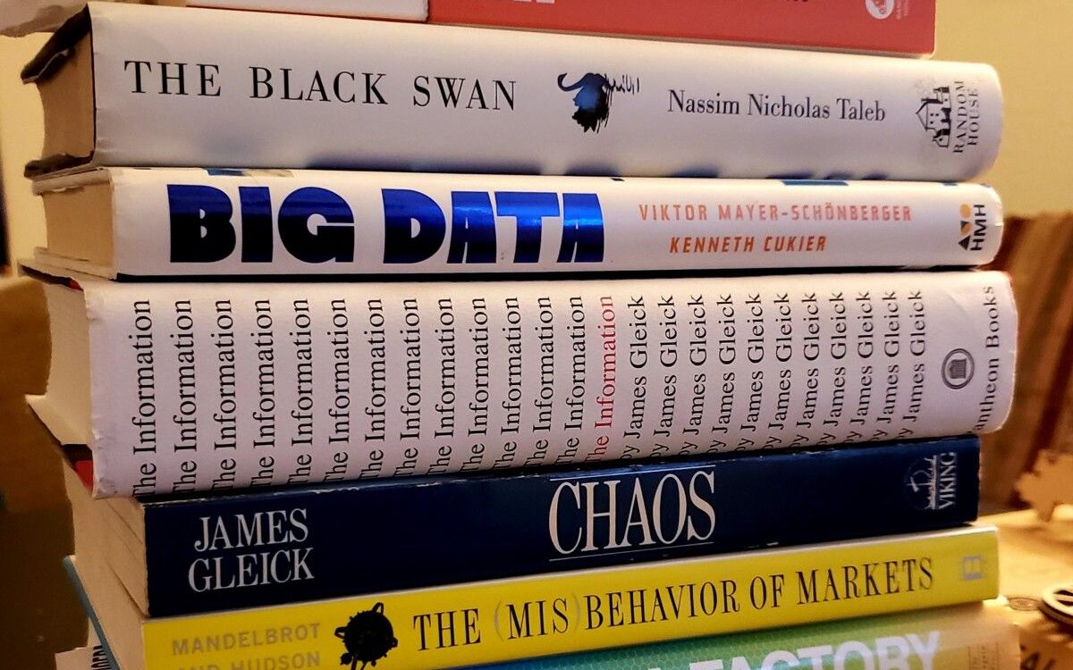 A stack of books on data, probability, and information, including The Black Swan, Big Data, The Information, and Chaos